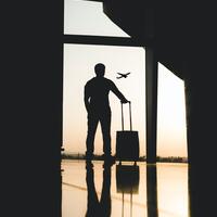 Man holding his suitcase in an airport with a plane in the background. 